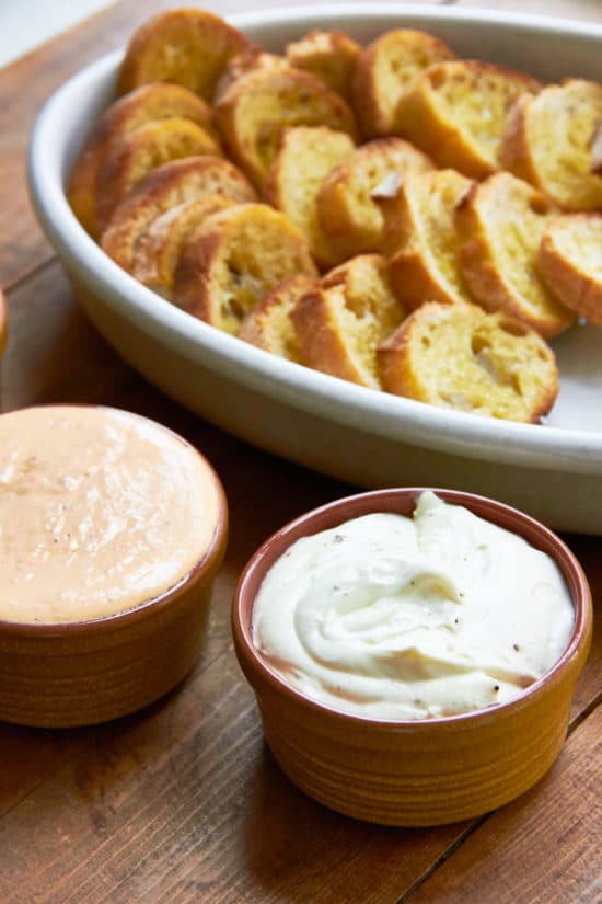 Differently colored Whipped Fresh Ricotta dips with slices of bread.