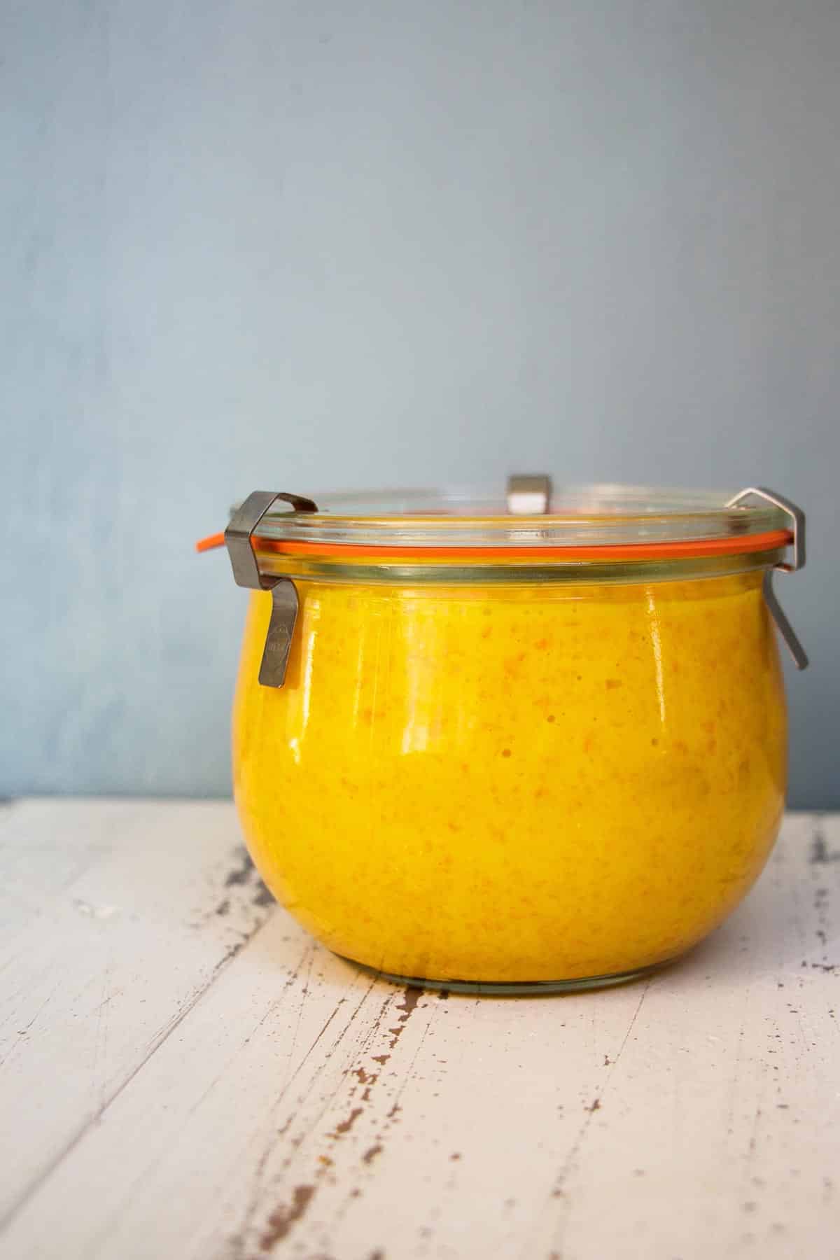 Jar of yellow carrot and ginger salad dressing on wood table.