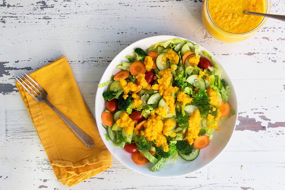 Fresh veggie salad on plate topped with yellow dressing on wood table.