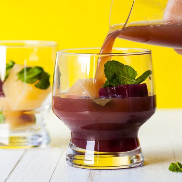 Pouring Pomegranate Orange Mocktail into glass with mint.