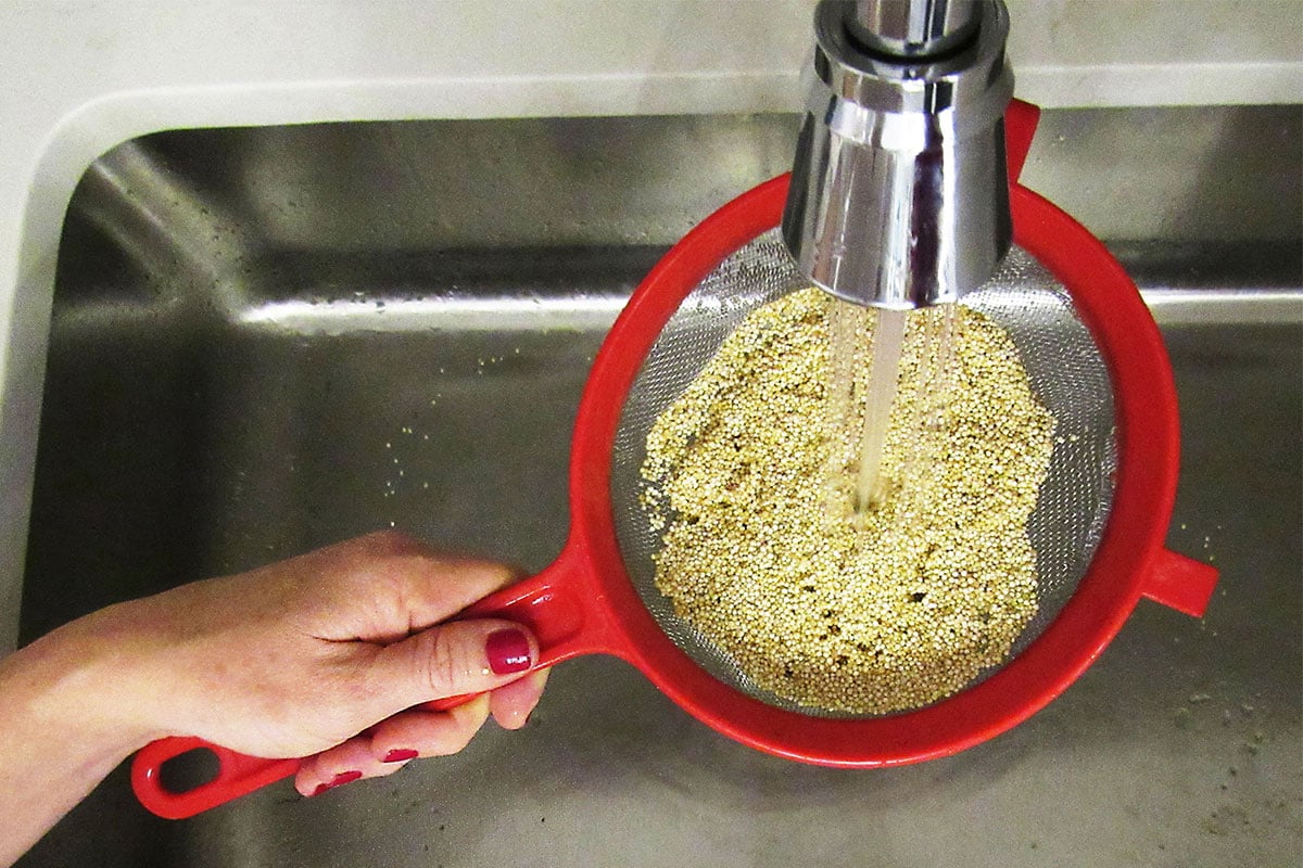 Woman rinsing quinoa in a sieve over a sink.