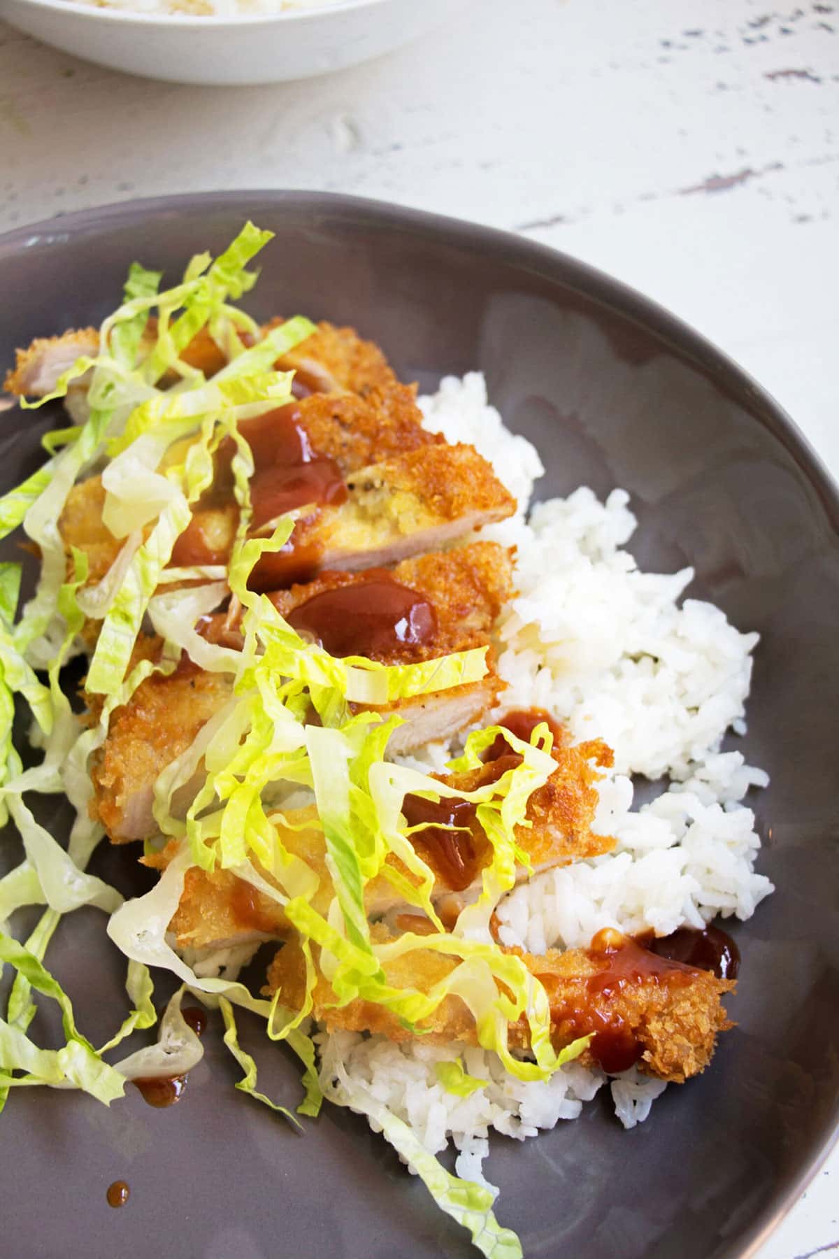 Sliced breaded chicken katsu on grey plate with rice and fresh cabbage.