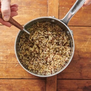 Fluffing quinoa with a fork in pan.