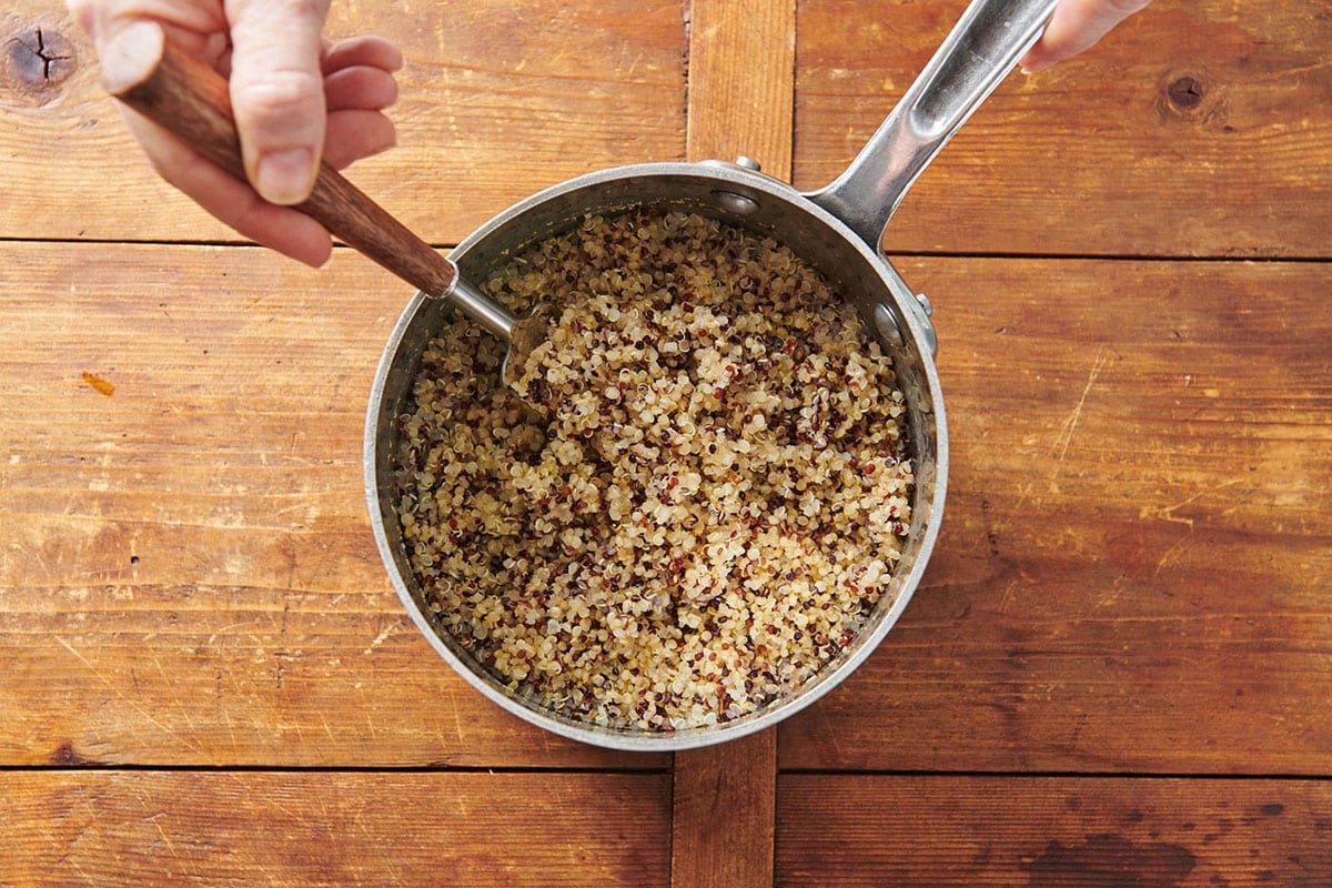 Fluffing quinoa with a fork in pan.