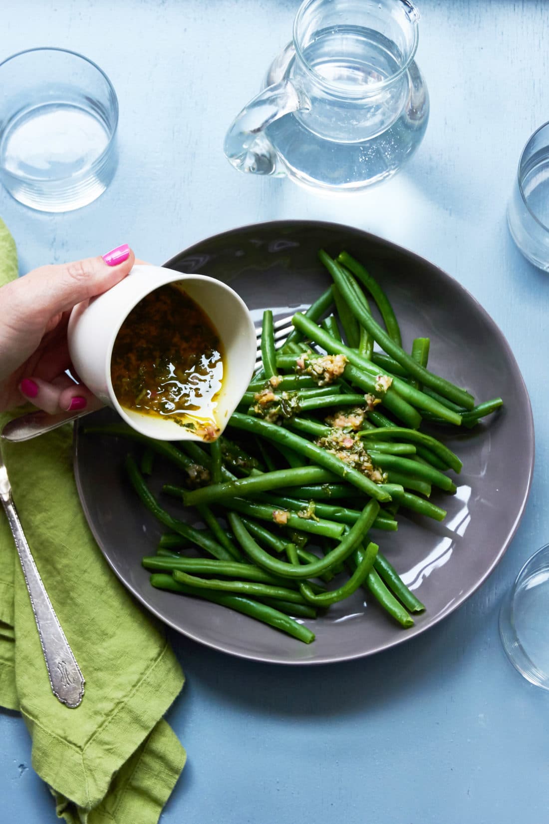 Woman pouring Tarragon Vinaigrette over Green Beans.