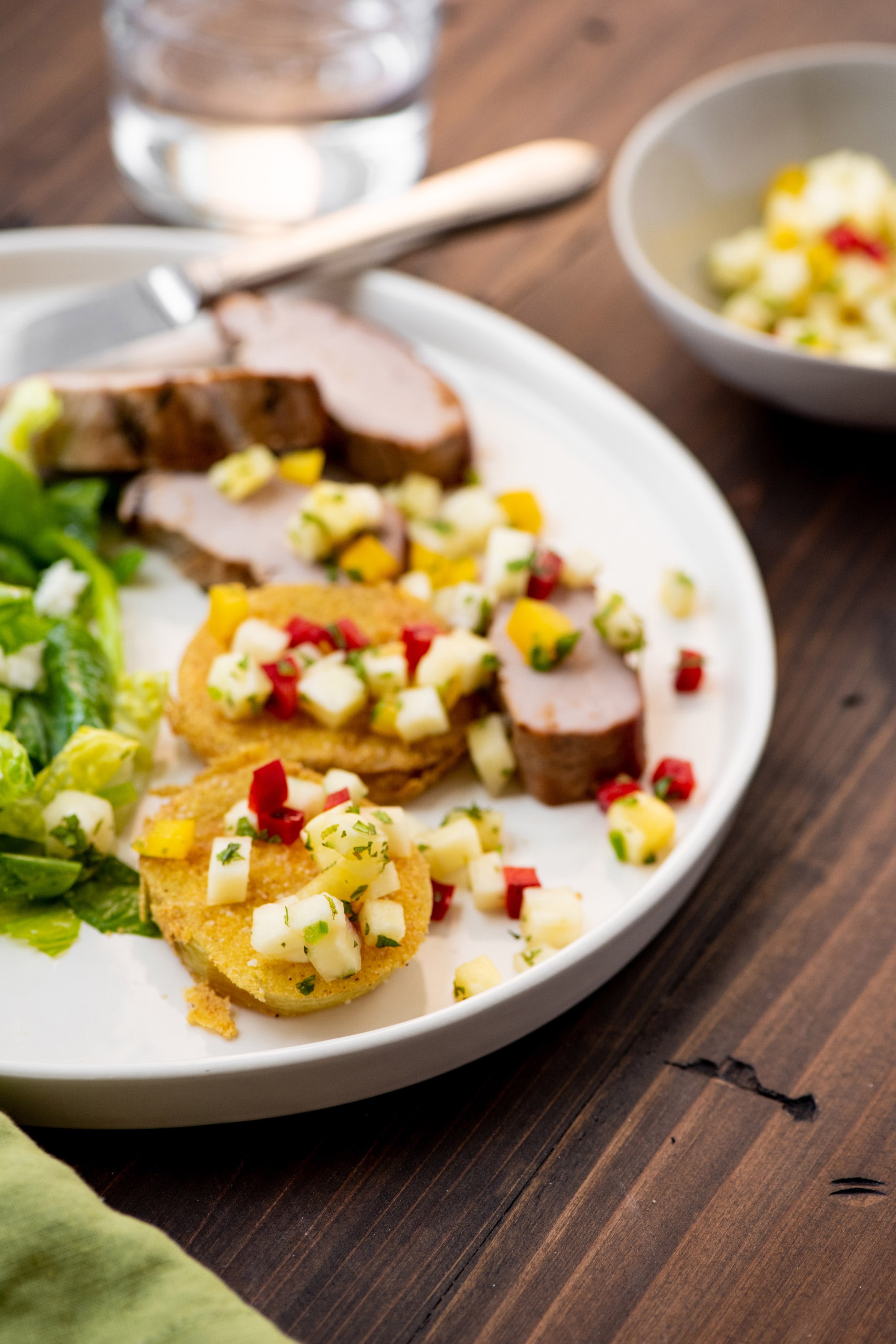 Pineapple-topped fried green tomatoes with sliced pork loin on plate.