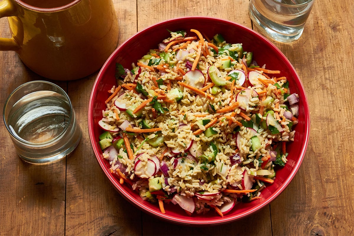 Vegetable and Brown Rice Salad with Honey Lemon Dressing in red bowl on table.