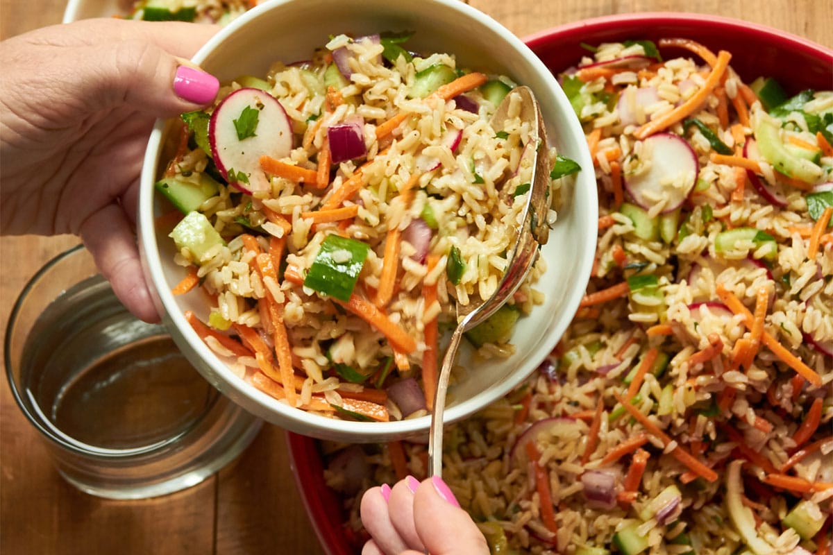 Woman scooping rice and vegetable salad into serving bowls.