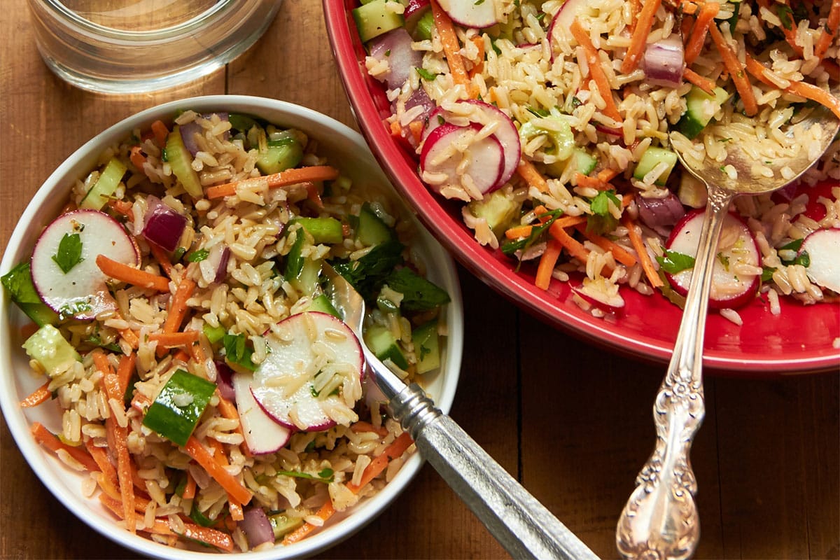 Table set with bowls of brown rice and veggie salad with water.