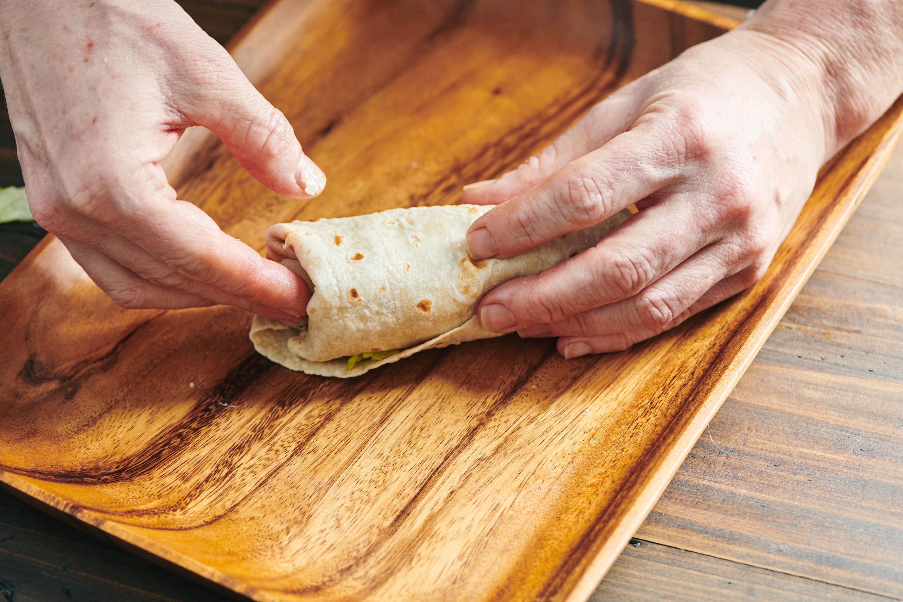 Woman tucking part of a tortilla into the end of a wrap.