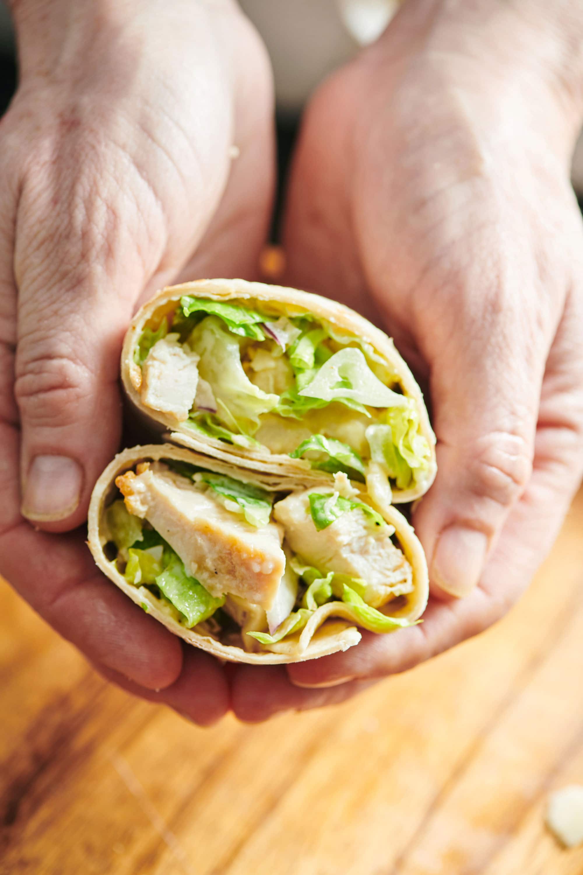 Woman hold a Grilled Chicken Caesar Salad Wrap cut in half.