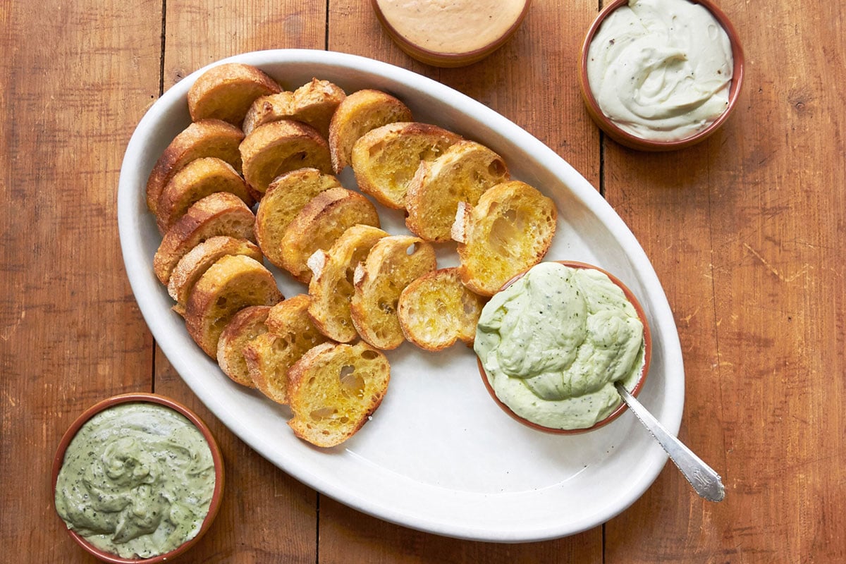 Basil and other flavored whipped ricottas in bowls on table with crostini.