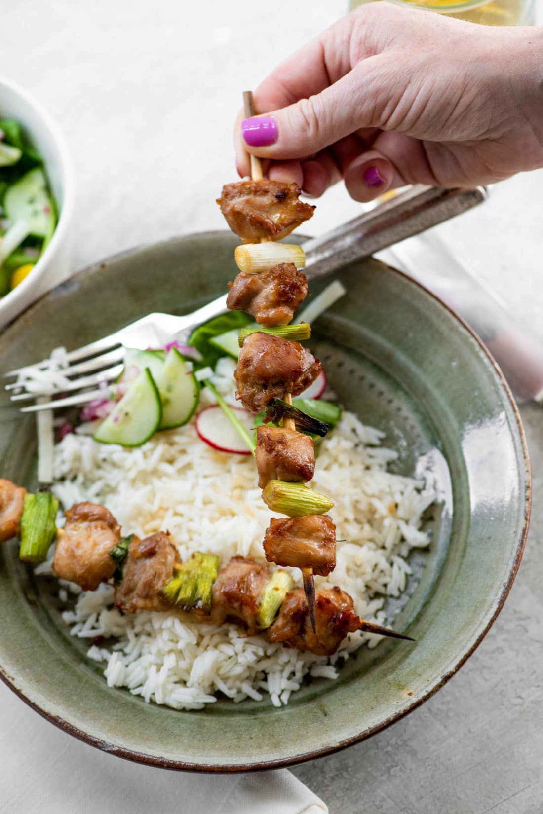 Woman holding a Chicken Yakitori skewer over a plate of rice.