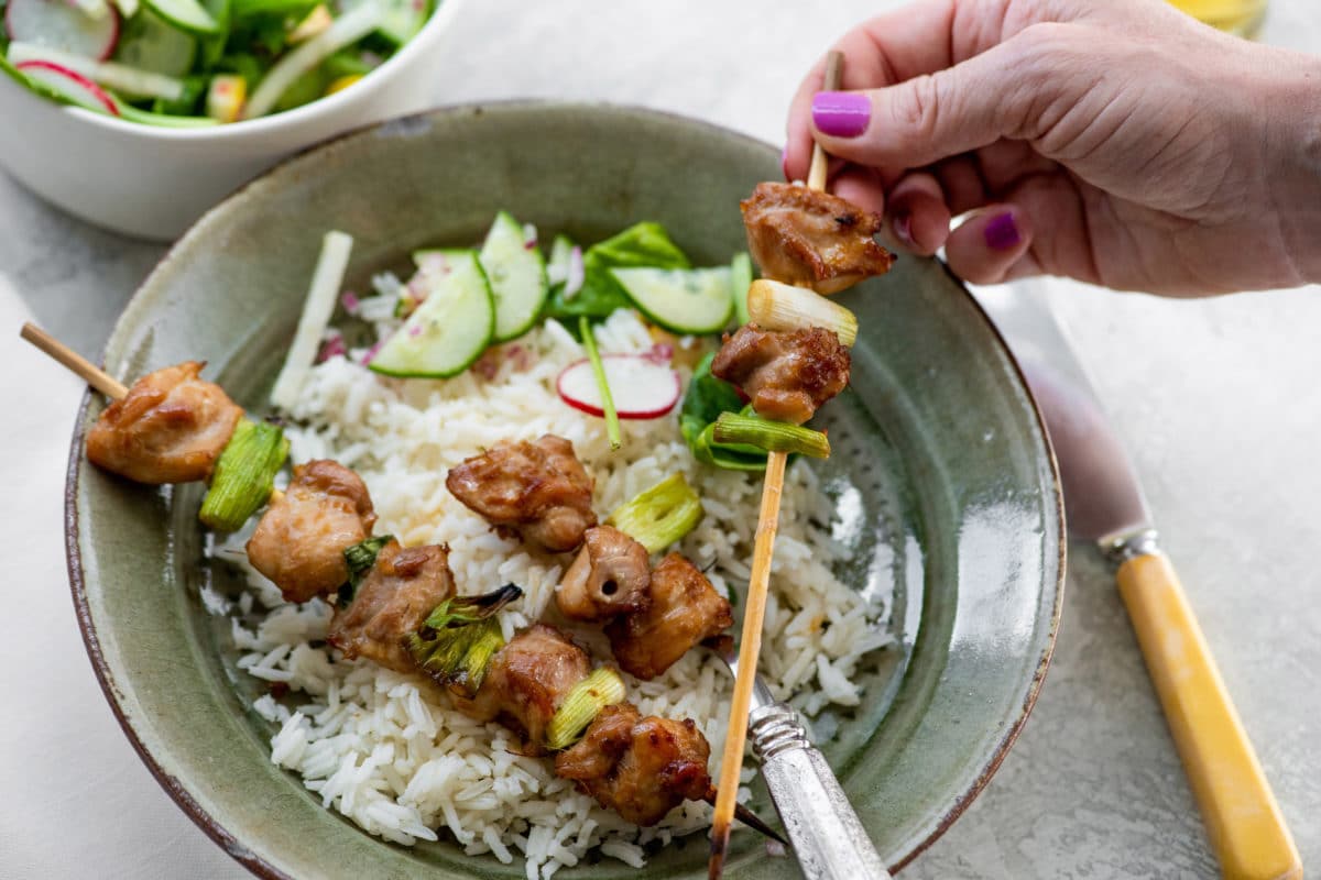 Woman removing Chicken Yakitori from a skewer onto a bed of rice.