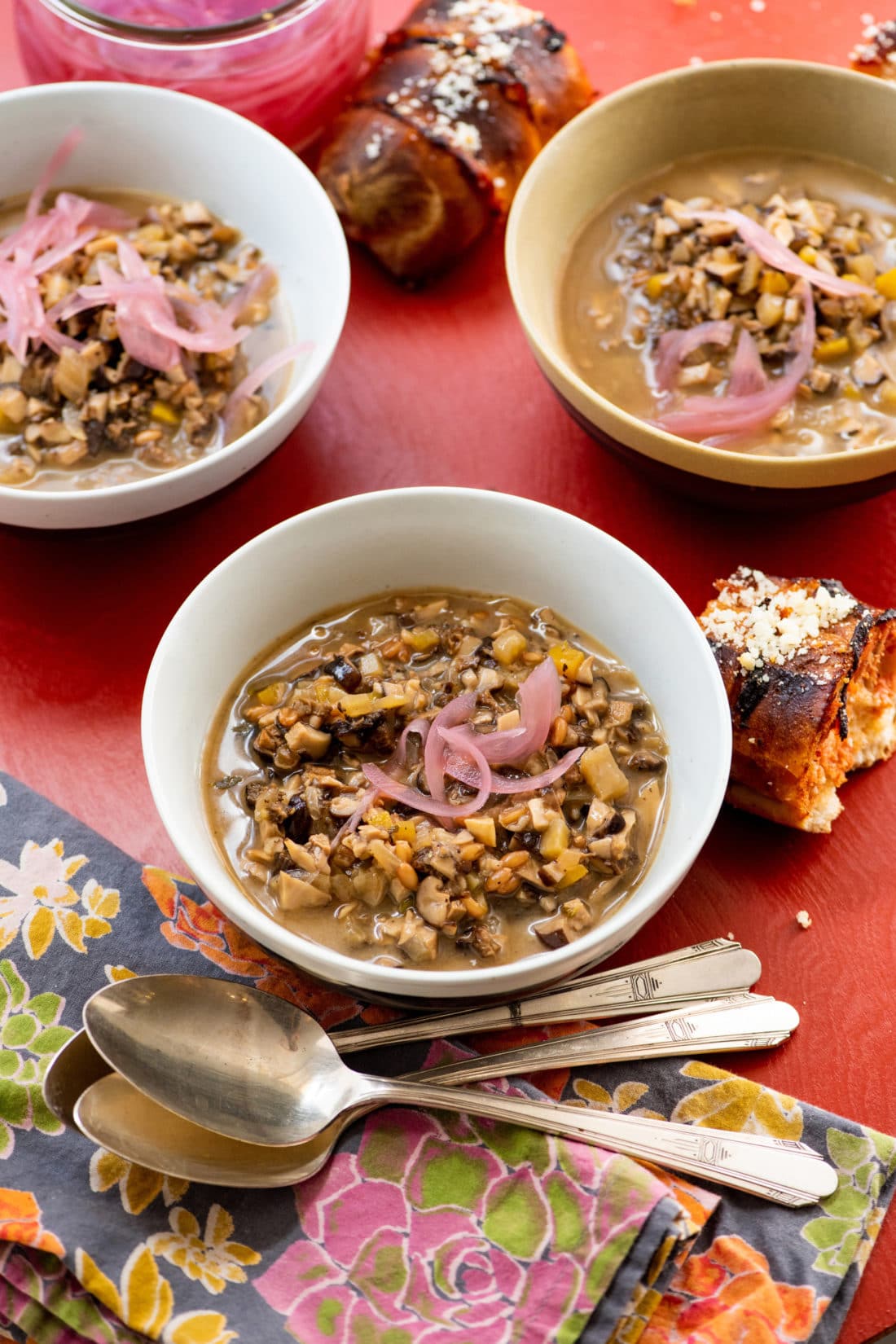 Spoons on a table with bowls of Mushroom Spelt Soup.