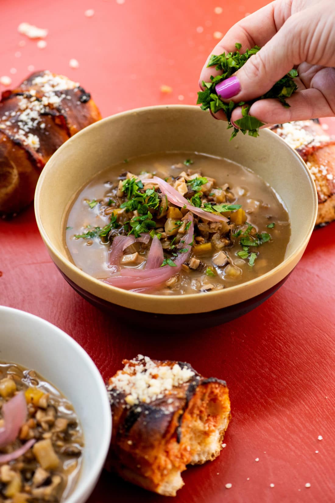 Woman sprinkling parsley on a bowl of Mushroom Spelt Soup.