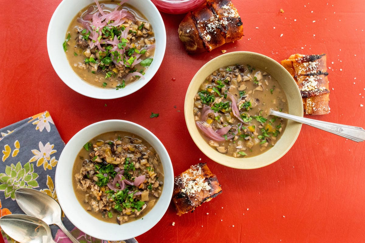 Three bowls of Mushroom Spelt Soup topped with parsley and pickled onions.
