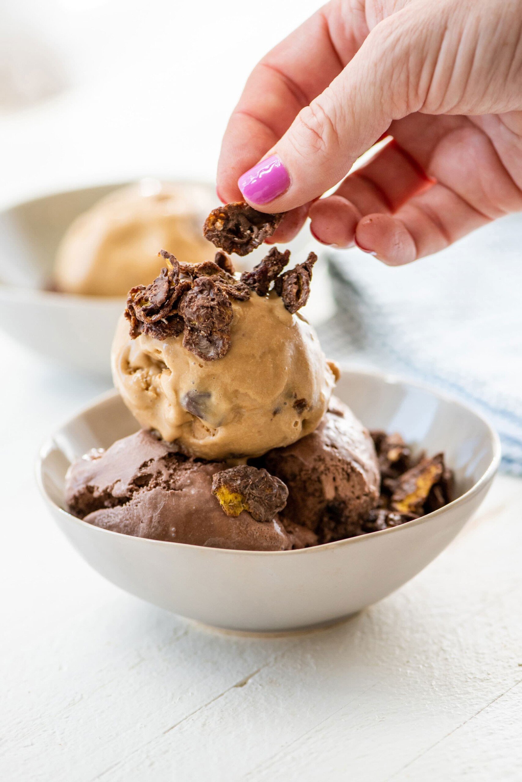 Woman placing Chocolate Peanut Cornflake Crunch on bowl of chocolate ice cream.