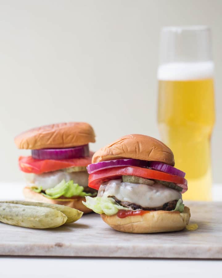 Deviled Burgers and pickles near a glass of beer.