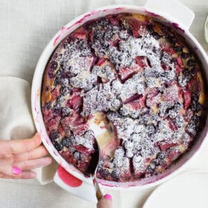 Woman using a spoon to scoop Summer Berry Clafoutis from a dish.