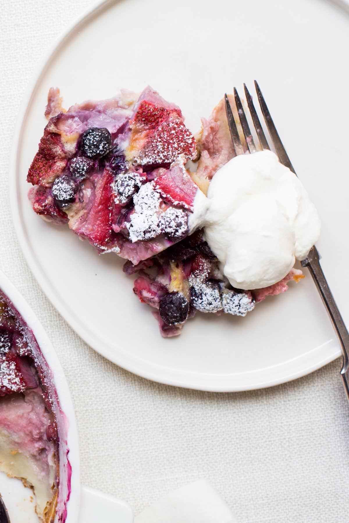 Berry Clafoutis  on plate with whipped cream and fork.