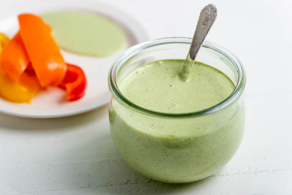 Green Goddess Dressing in a glass jar with a spoon.