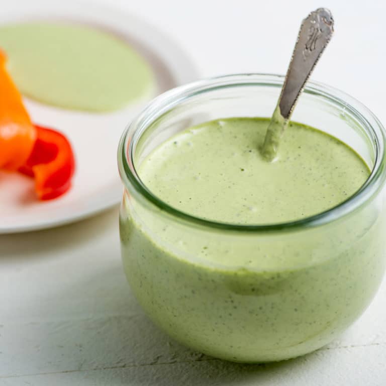 Green Goddess Dressing in a glass jar with a spoon.