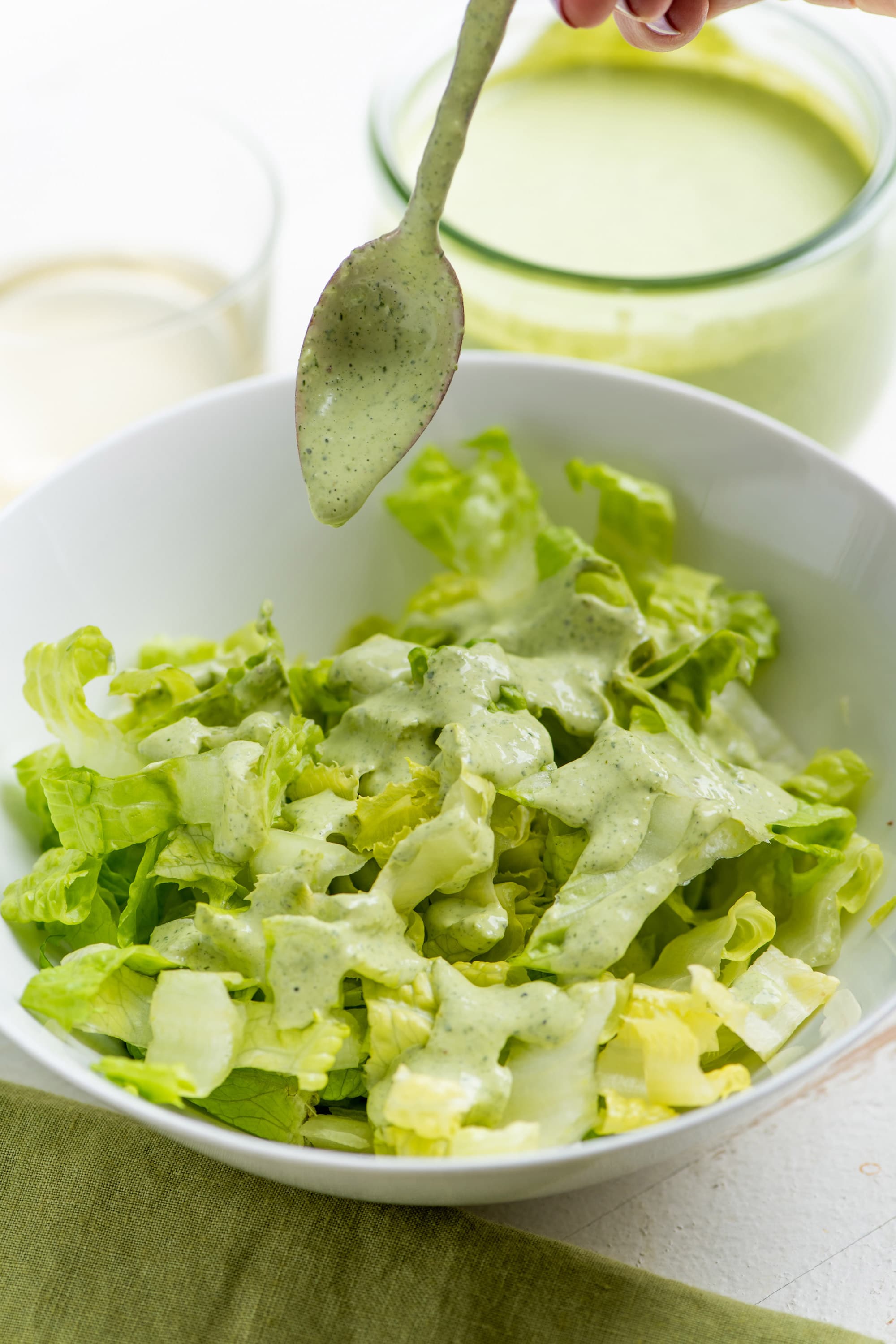 Spoon drizzling Green Goddess Dressing over a green salad.