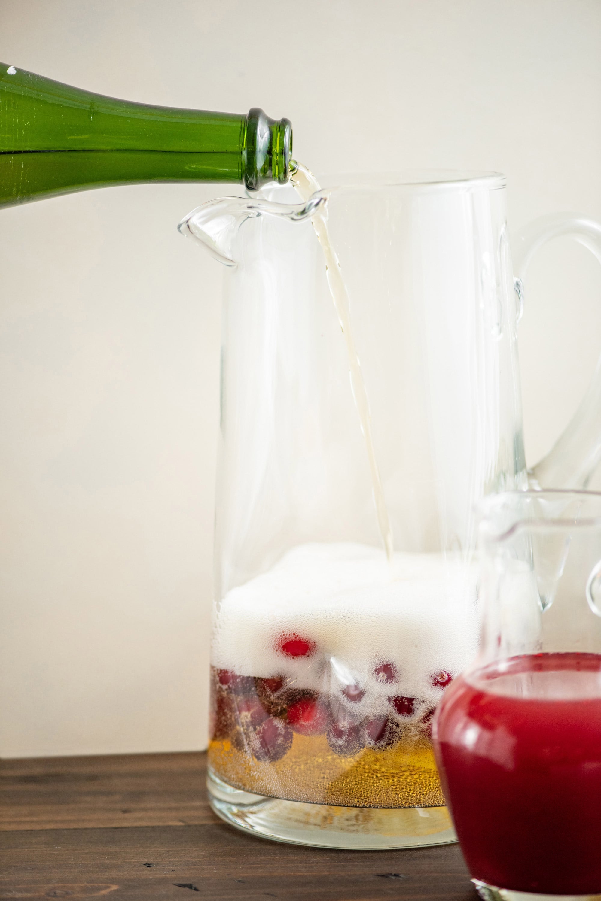 Sparking wine being poured into a pitcher with cranberries in it.