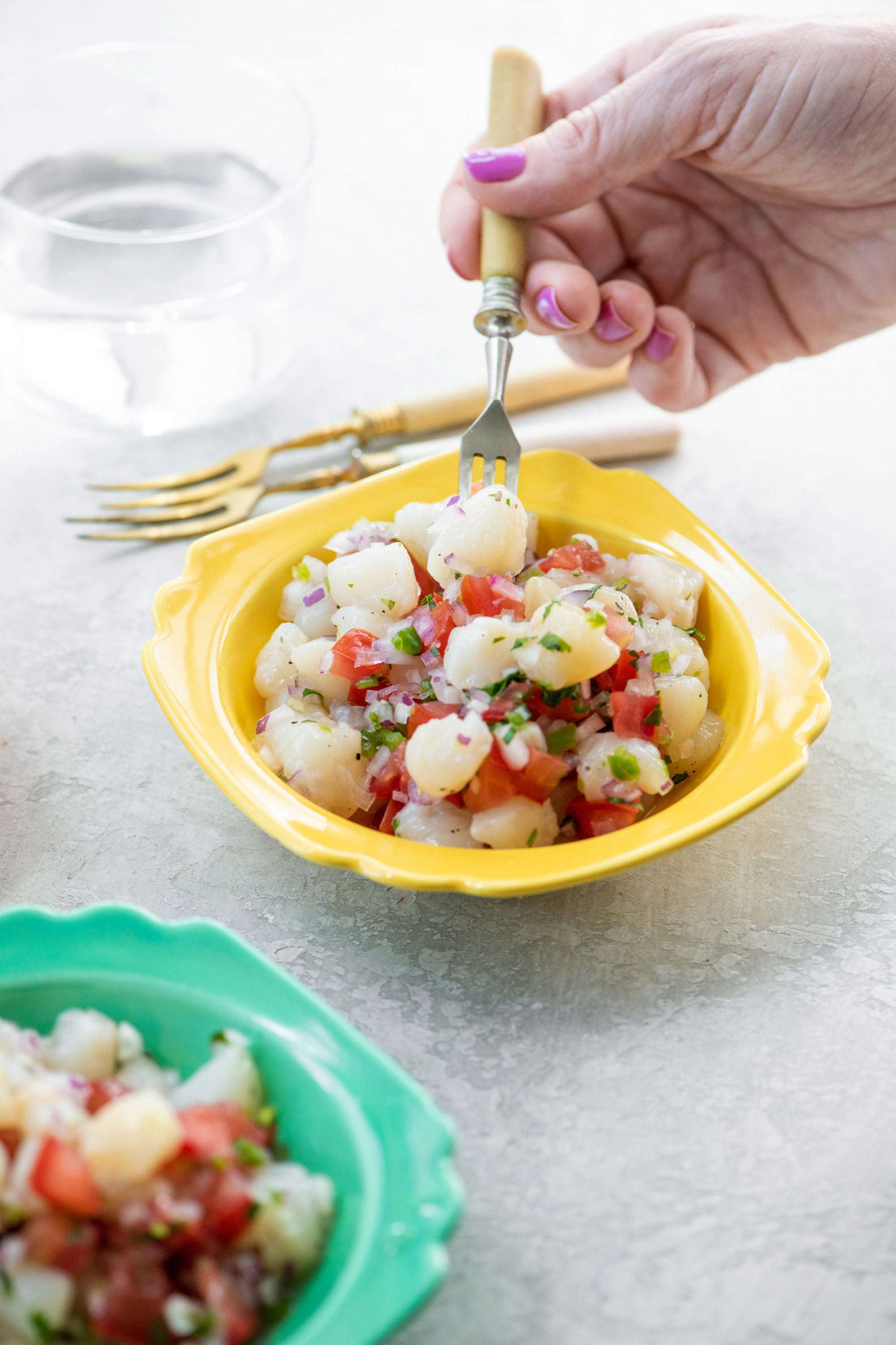 Woman scooping scallop ceviche from yellow bowl.