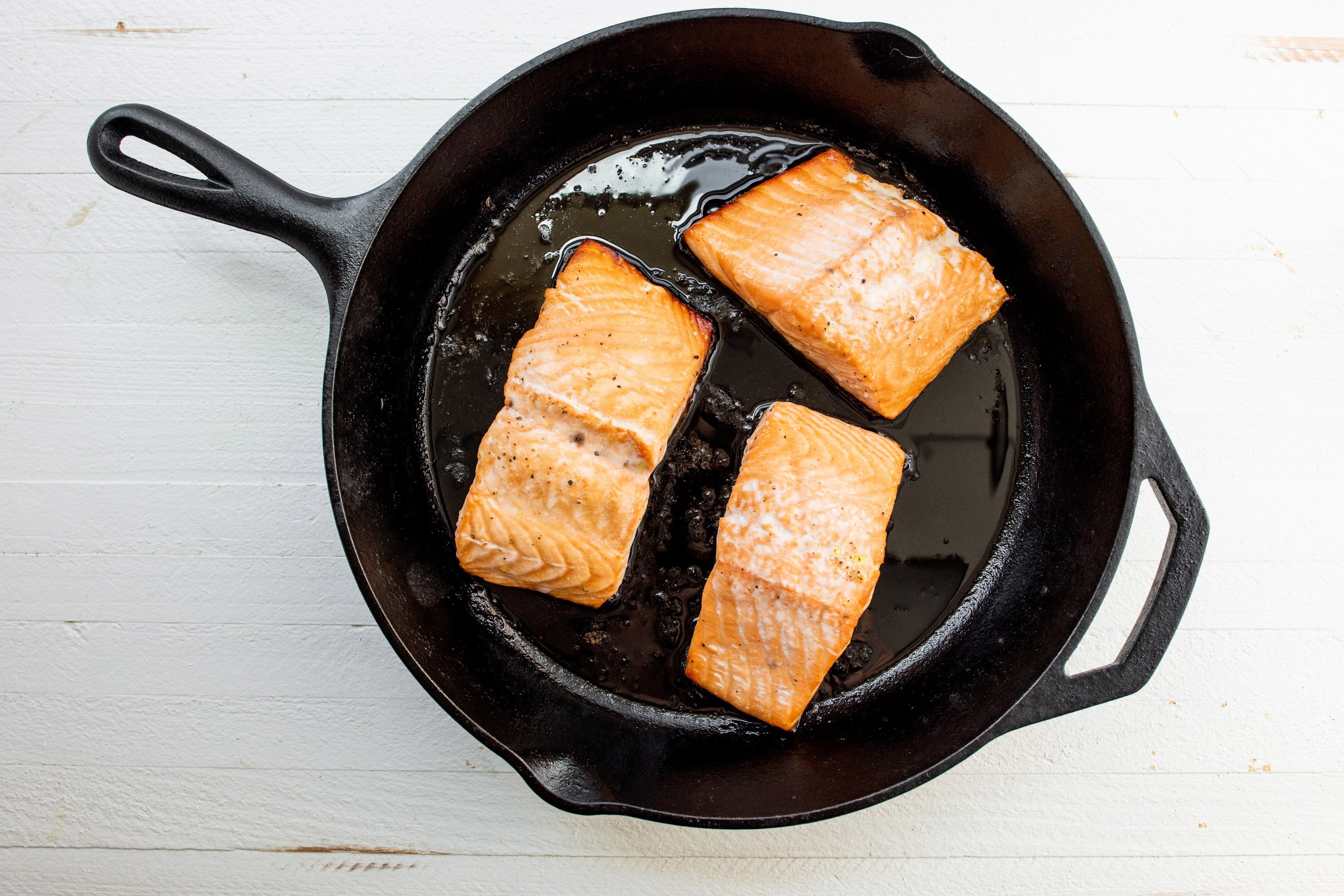 Three salmon filets in cast-iron pan.