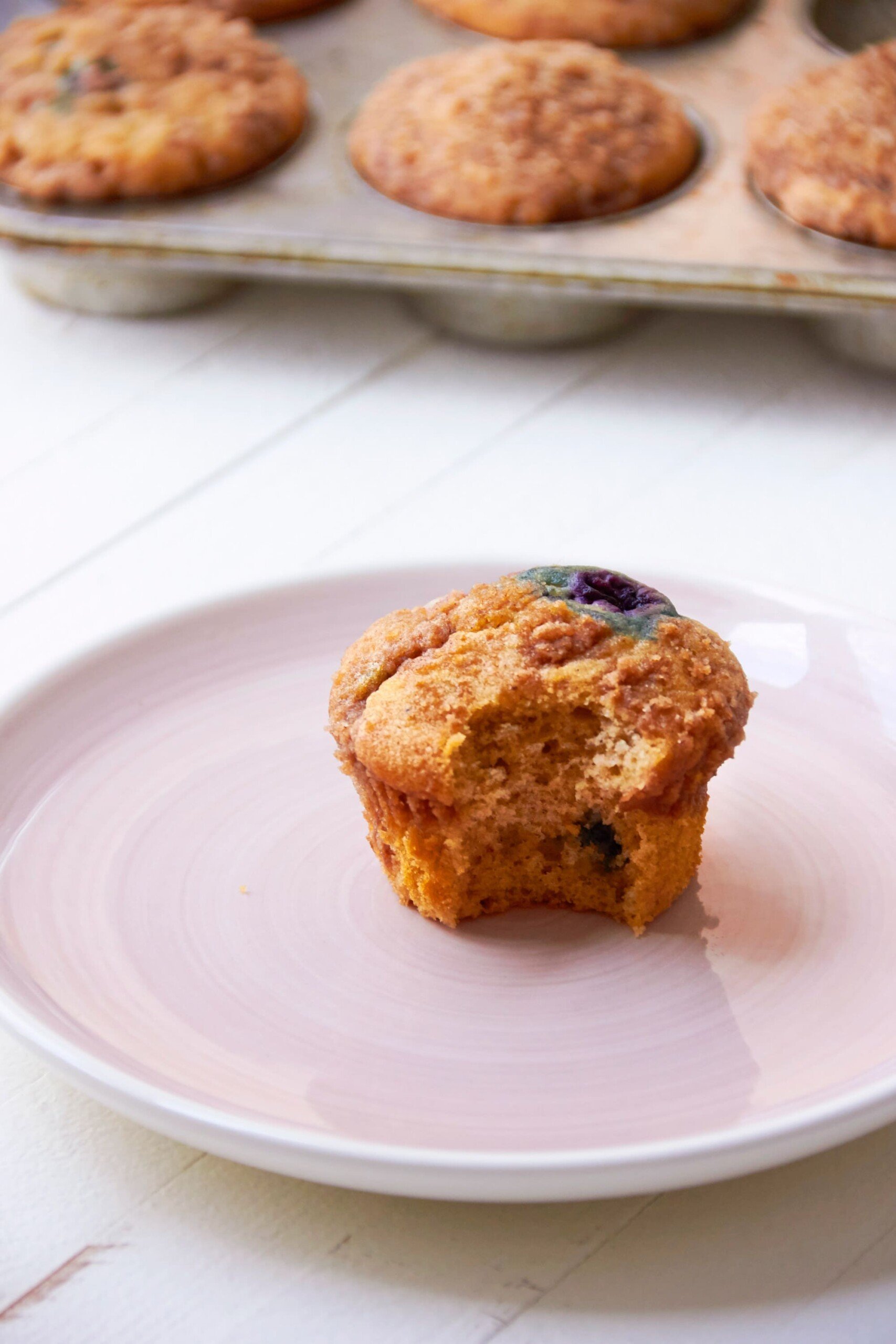 Berry Cinnamon Streusel Muffin on pink plate in front of muffin tin.