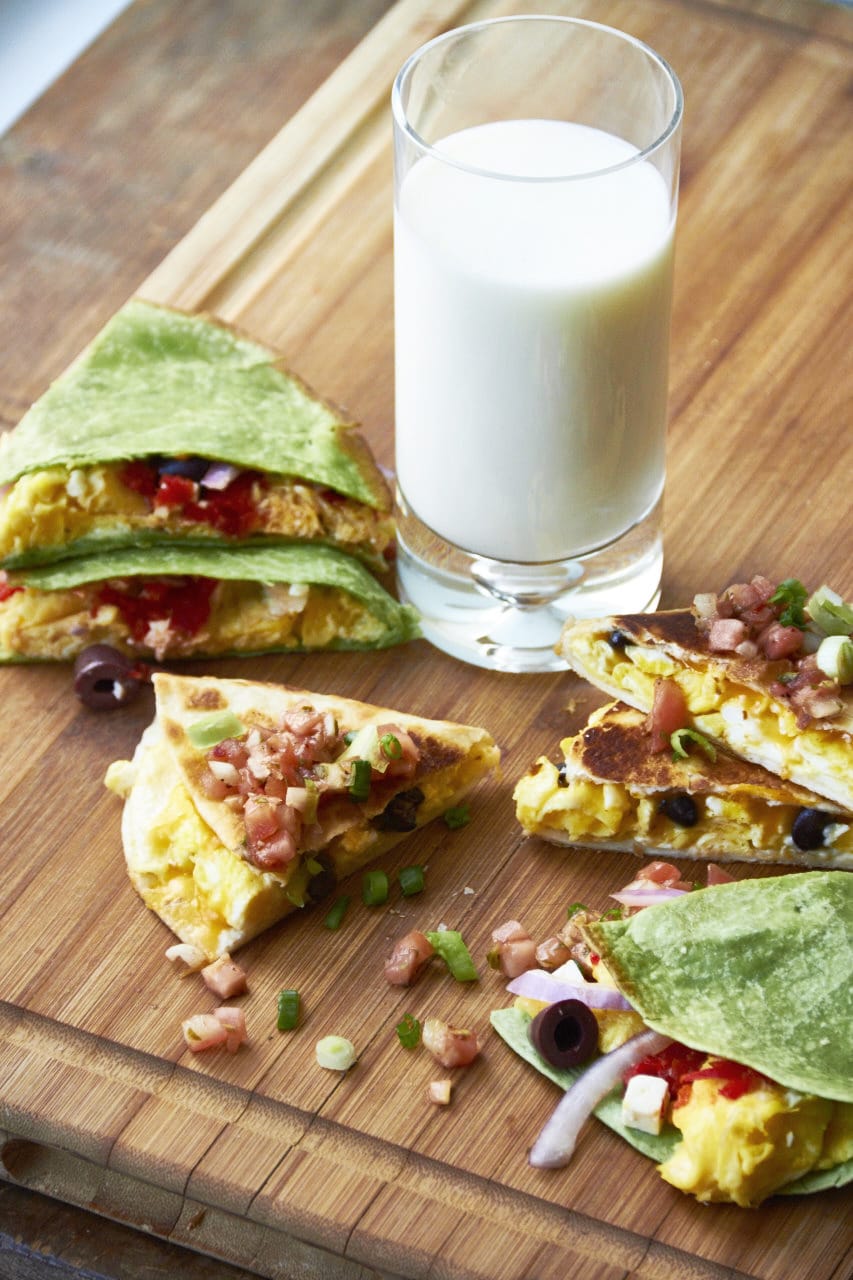 Breakfast quesadillas on a wooden cutting board with a glass of milk.
