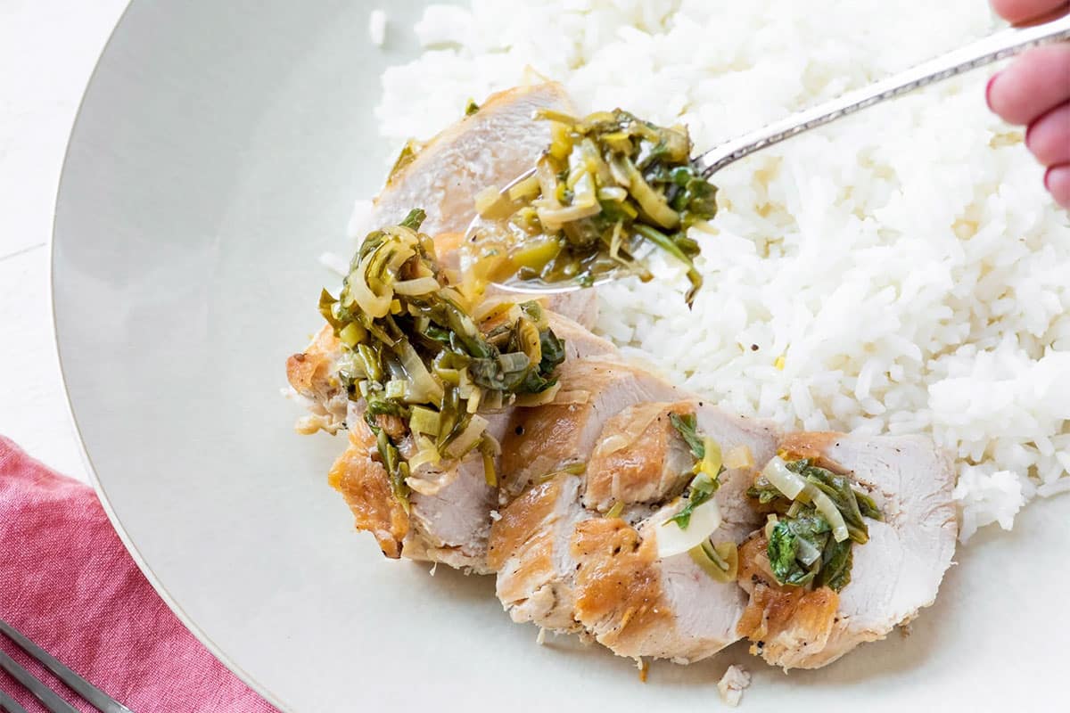 Topping pan sauce with vegetables over sliced chicken on plate with rice.