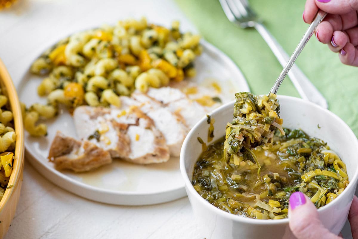 Serving white wine pan sauce with greens and leeks over sliced chicken.