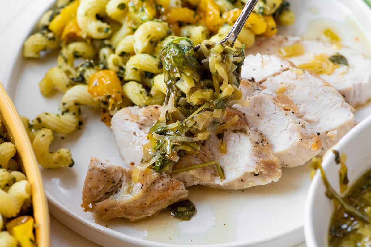 Topping pan sauce with vegetables over sliced chicken on plate with rice.