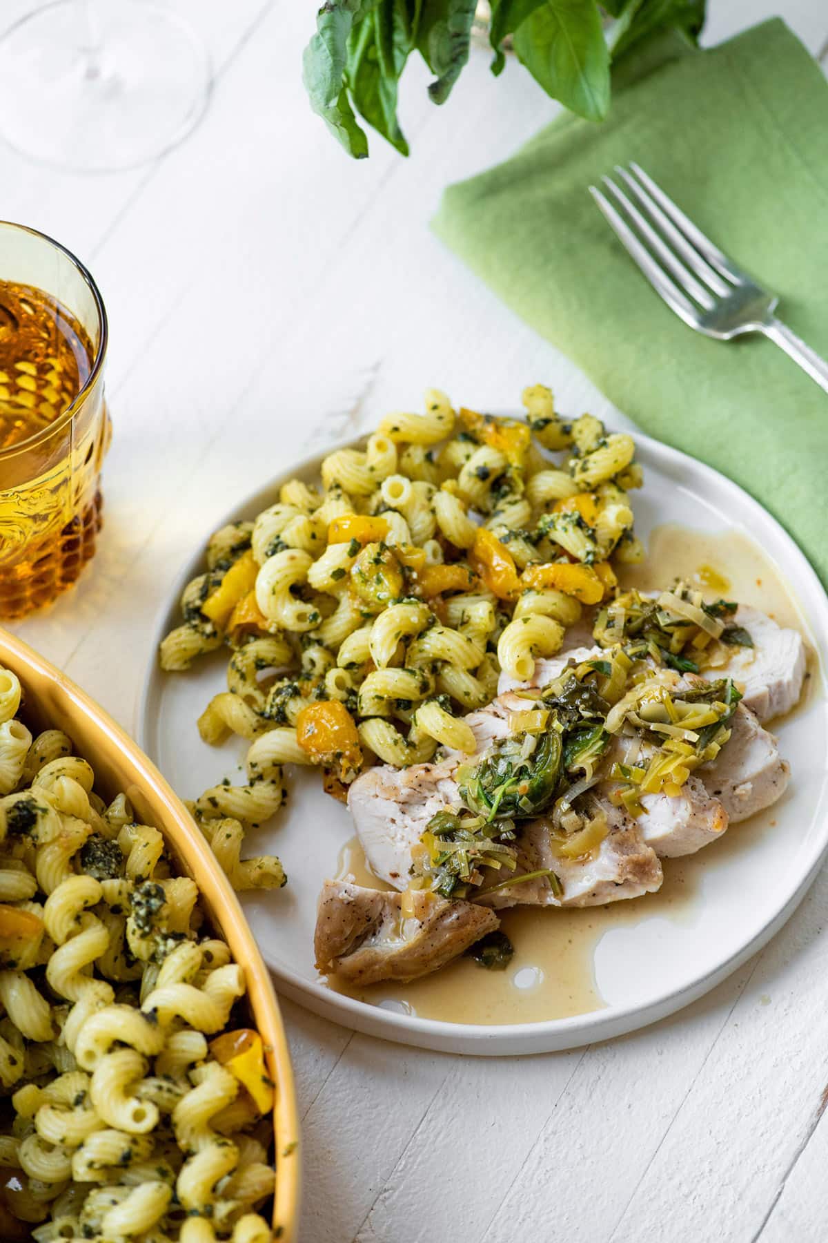Chicken in vegetable pan sauce on plate with pasta salad.