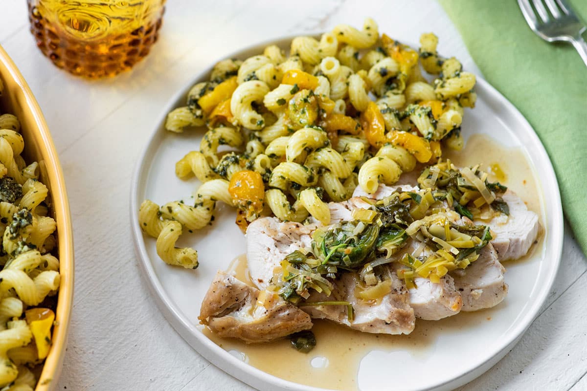 Chicken breasts covered in pan sauce on plate with pasta salad.