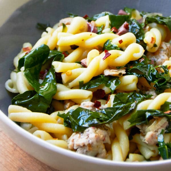 Campanelle pasta with chicken sausage and kale in bowl on table.