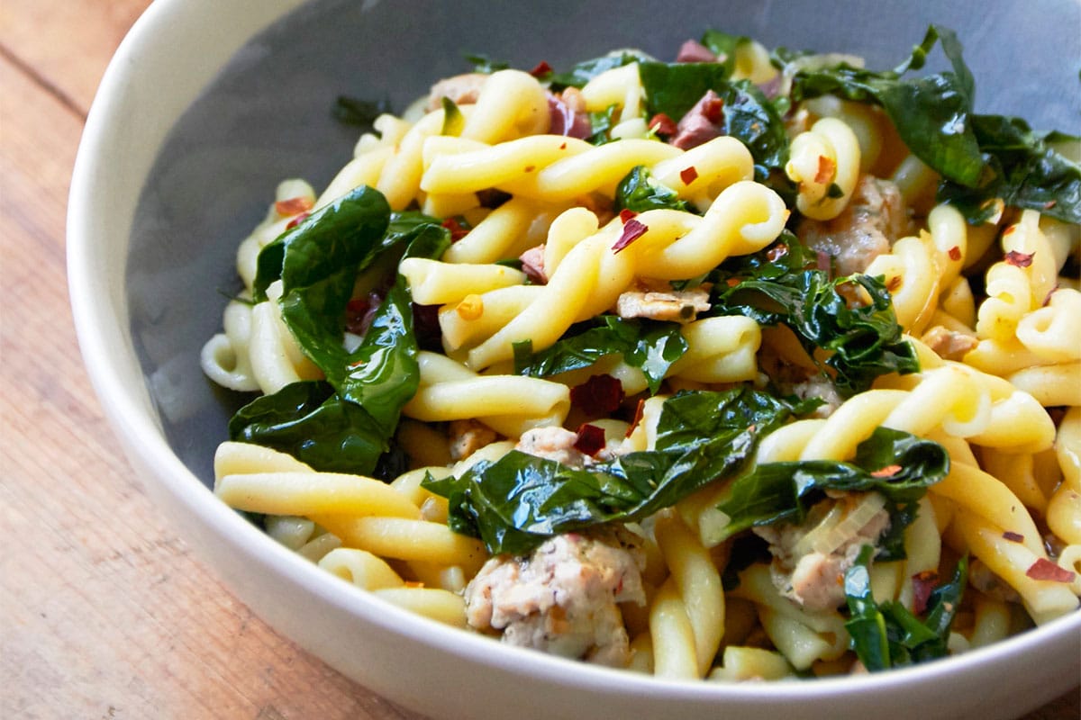 Campanelle pasta with chicken sausage and kale in bowl on table.