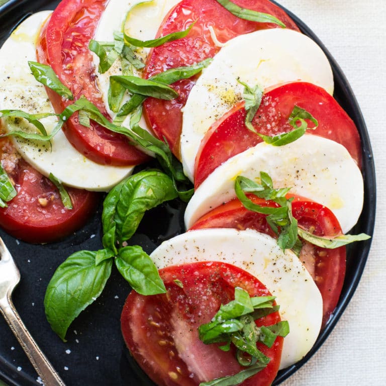 Alternating slices of mozzarella cheese and tomatoes topped with seasonings and basil.