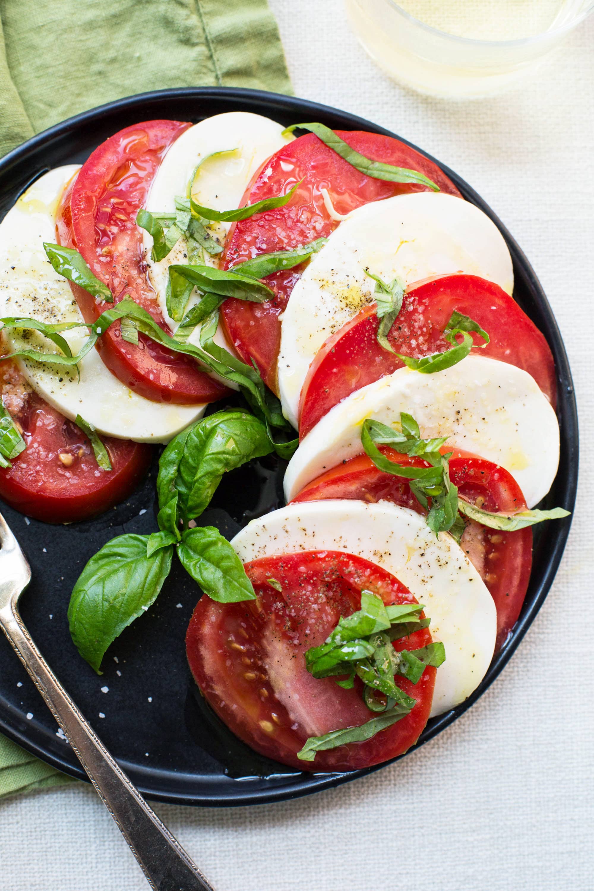 Alternating slices of mozzarella cheese and tomatoes topped with seasonings and basil.