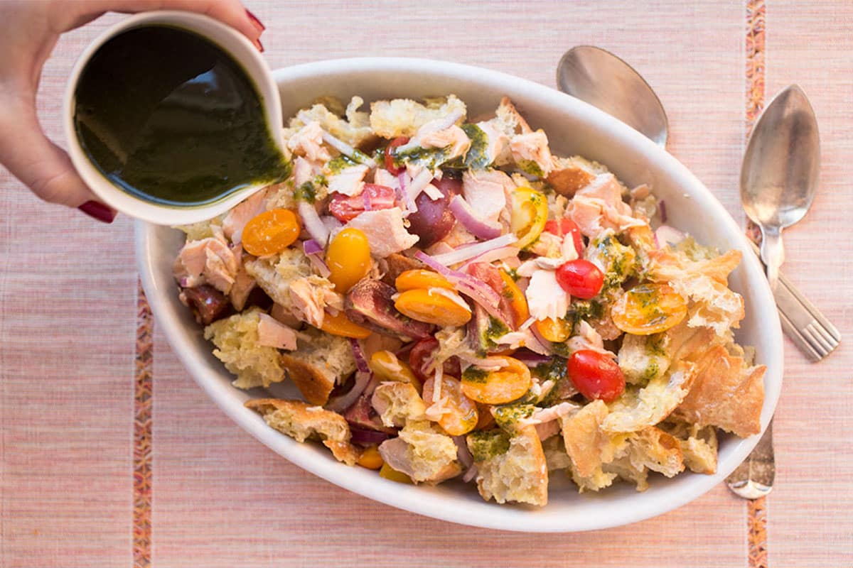 Pouring basil oil over salmon panzanella in serving dish.