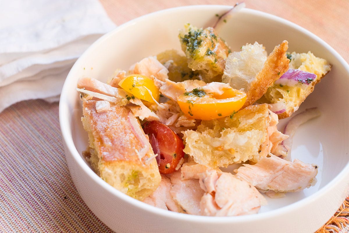 Small white bowl with Salmon Panzanella on table.