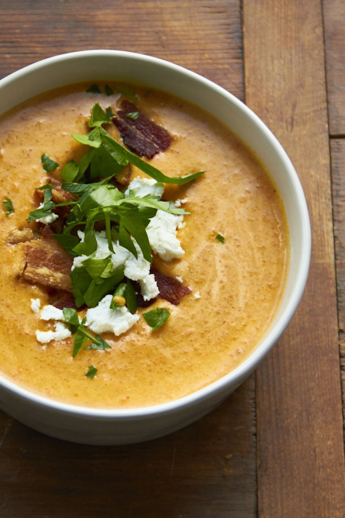 Cream of Carrot Soup in a white bowl with parsley, feta and crispy bacon bits.