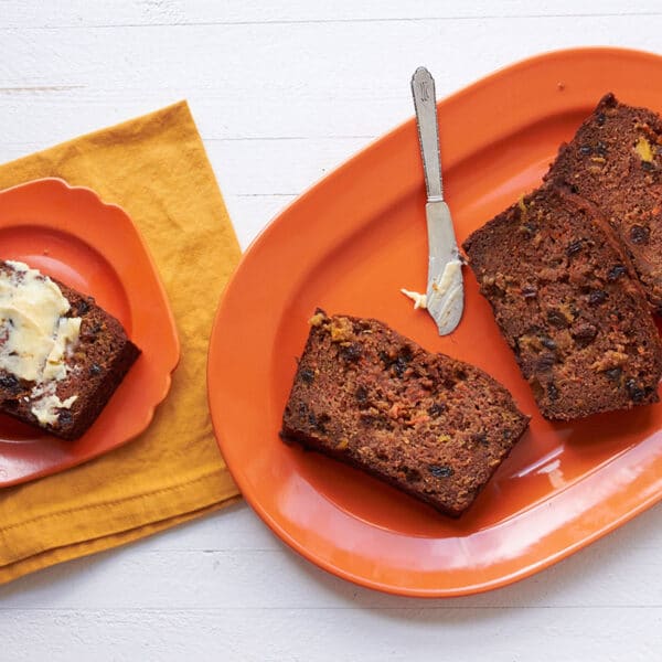 Carrot Raisin Bread sliced on orange plates with knife and butter.