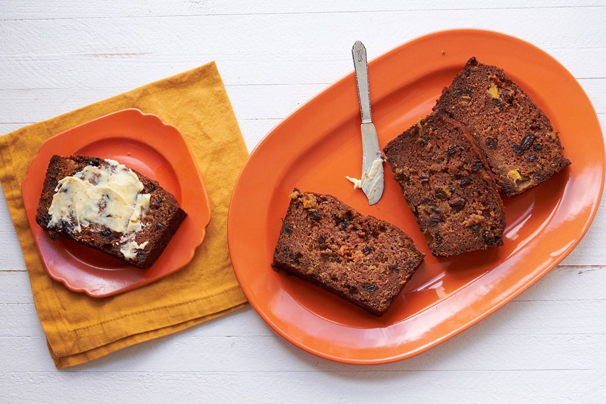 Carrot Raisin Bread sliced on orange plates with knife and butter.