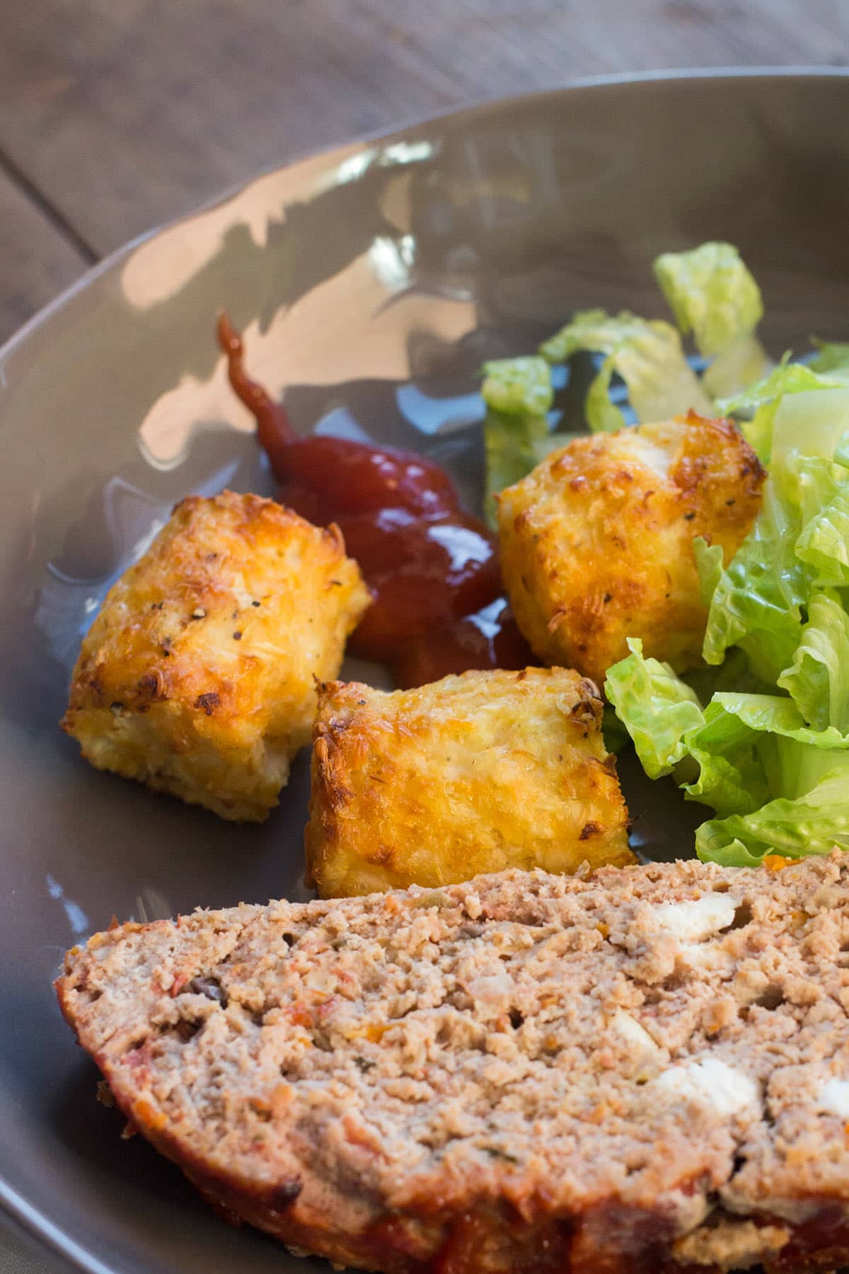 Grey plate with meatloaf, cauliflower tots, and salad.