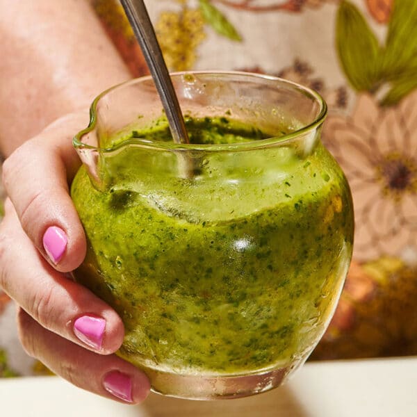 Woman holding jar of persillade sauce with spoon.