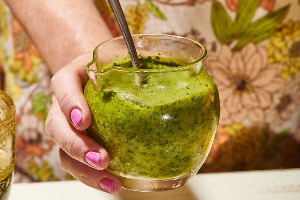 Woman holding jar of persillade sauce with spoon.